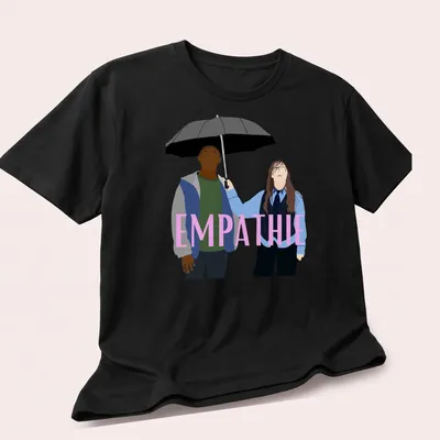 Flat design of two figures sharing an umbrella with the word 'EMPATHIE' above them — printed on a unisex t-shirt (angled view)