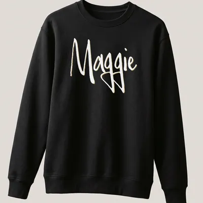 Elegant script design with the name Maggie in gold on a white background — printed on a unisex sweatshirt