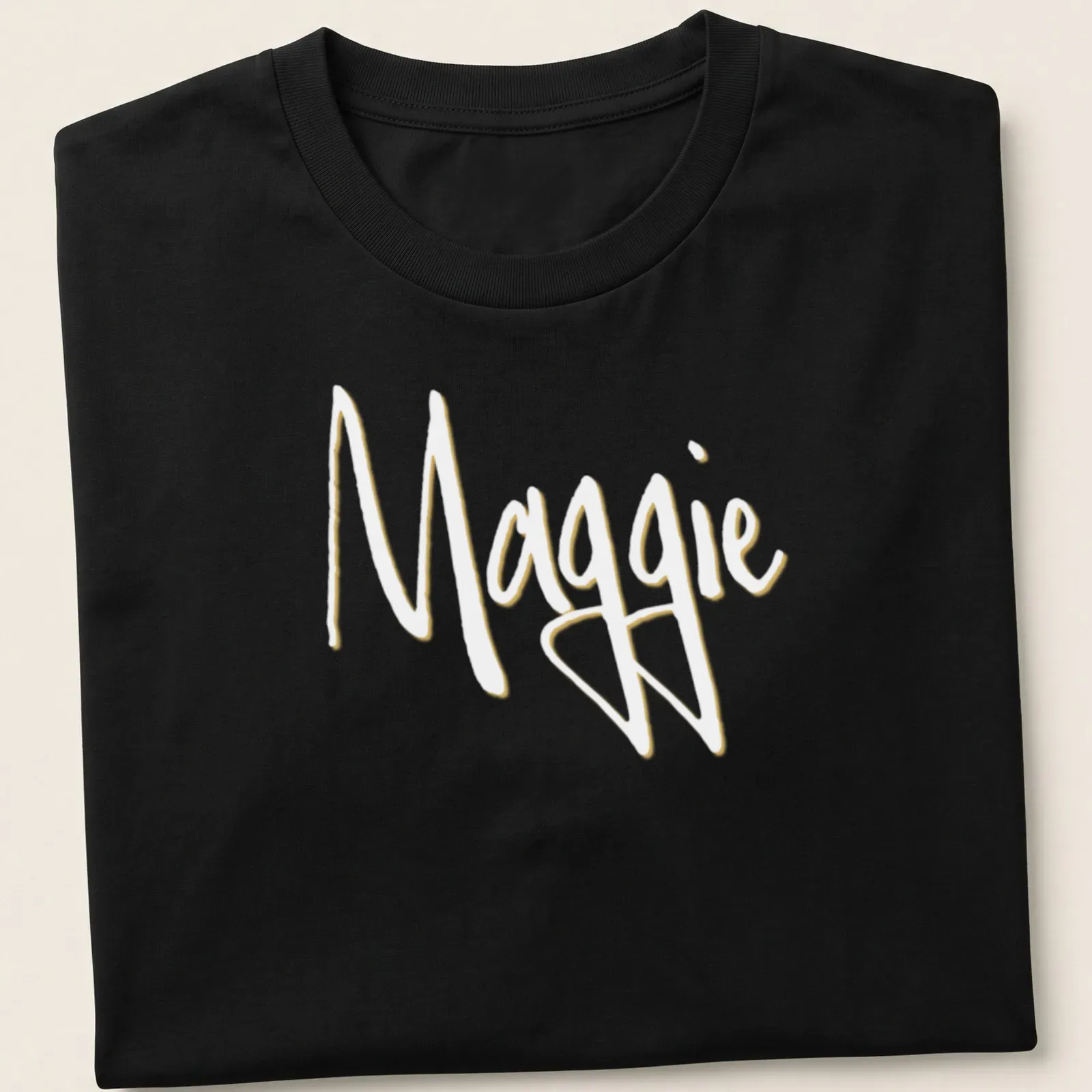 Elegant script design with the name Maggie in gold on a white background — printed on a unisex t-shirt