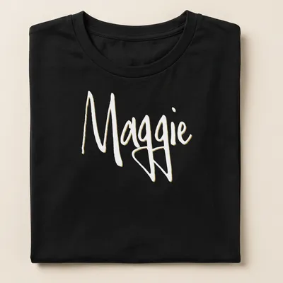 Elegant script design with the name Maggie in gold on a white background — printed on a women's shirt