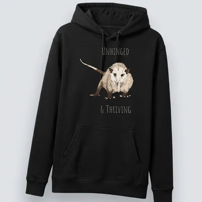 Sketch illustration of an opossum with the text 'UNHINGED & THRIVING' in earthy colors — printed on a unisex hoodie