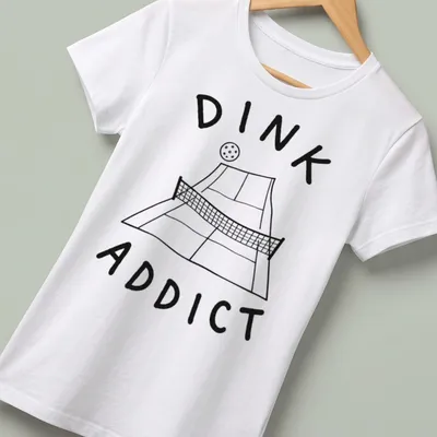 Line-art pickleball court with bold text 'DINK ADDICT' in black and white — printed on a women's shirt