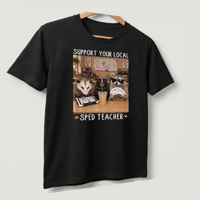Photorealistic raccoon holding an apple with text supporting SPED teachers — printed on a unisex t-shirt (angled view)