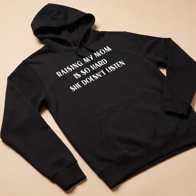 Bold text t-shirt reading 'Raising My Mom Is So Hard She Doesn't Listen' in white. — printed on a unisex hoodie