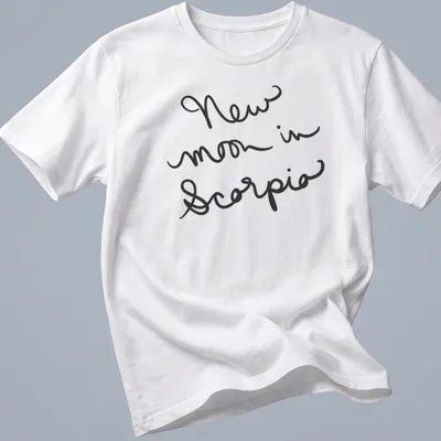 Black shirt with handwritten text 'New moon in Scorpio' in elegant script.