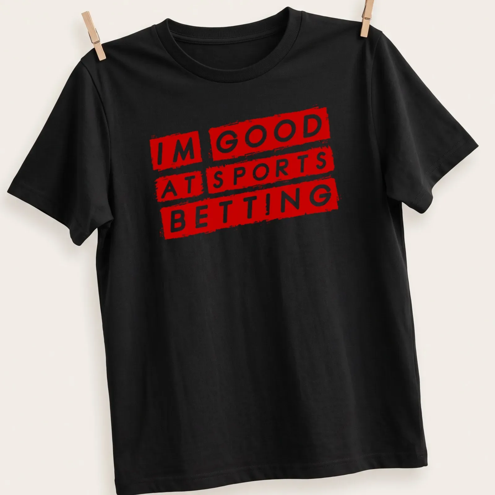 Bold graphic t-shirt featuring the phrase 'I'm Good At Sports Betting' in red and white — printed on a unisex t-shirt