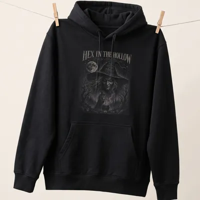 Gothic witch brewing potion design with the text 'HEX IN THE HOLLOW Brewed After Midnight' — printed on a unisex hoodie
