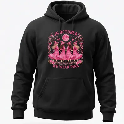 Whimsical illustration of witch sisters with text 'In October We Wear Pink' in pink tones. — printed on a unisex hoodie