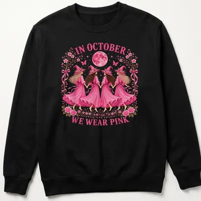 Whimsical illustration of witch sisters with text 'In October We Wear Pink' in pink tones. — printed on a unisex sweatshirt